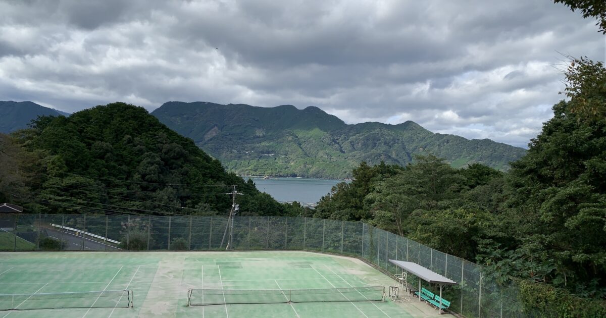山と湖を望む曇り空のテニスコート