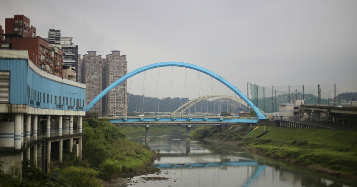 曇り空の下に架かる青いアーチ橋と都市の風景