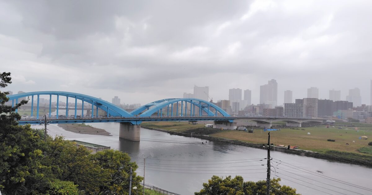 雨空の下に架かる青いアーチ橋と都市景観