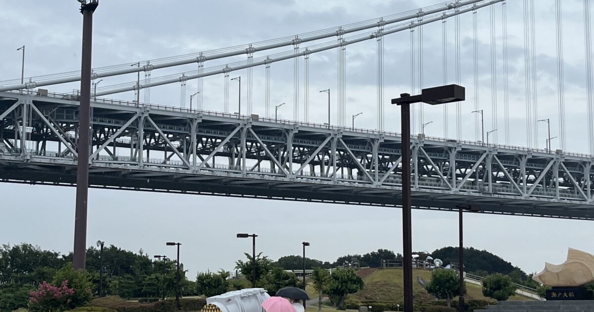 雨の中傘を差して歩く人と大きな吊り橋の風景