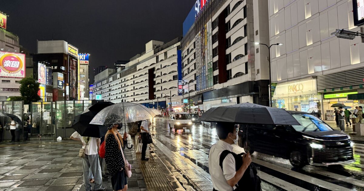 夜の雨の中で傘を差す人々と濡れた都市の街並み