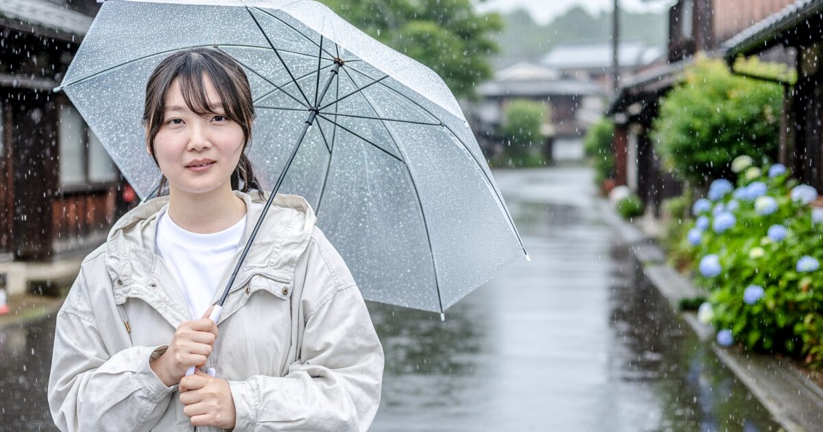 雨の中で透明な傘を差す女性と古い街並み