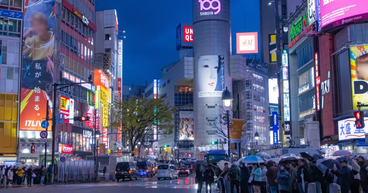 夜の渋谷で傘を差す人々とネオンの街並み