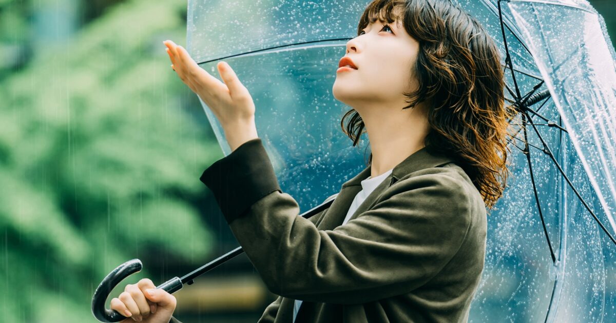雨の中で空を見上げる女性と透明な傘