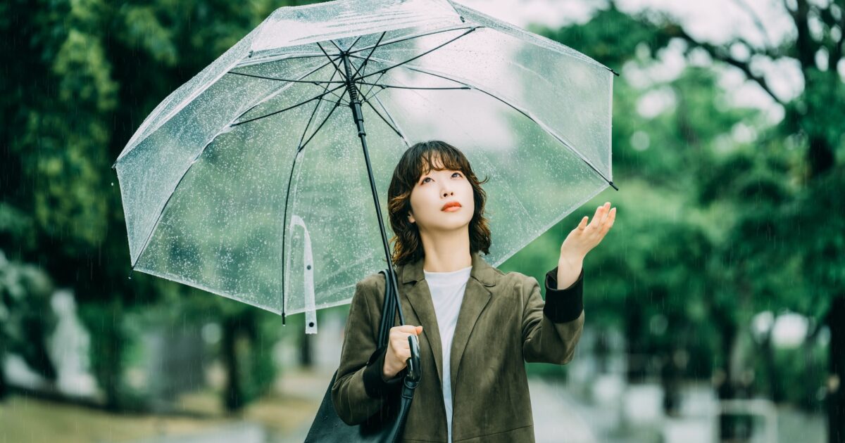 雨の中で透明な傘を差す女性と公園の風景