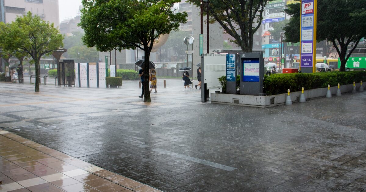 雨が降る駅前の街並みと傘を差す人々
