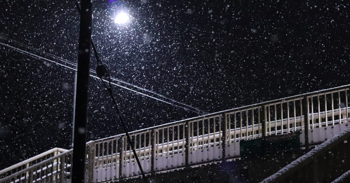 雪が舞う夜の街灯と歩道橋のシルエット