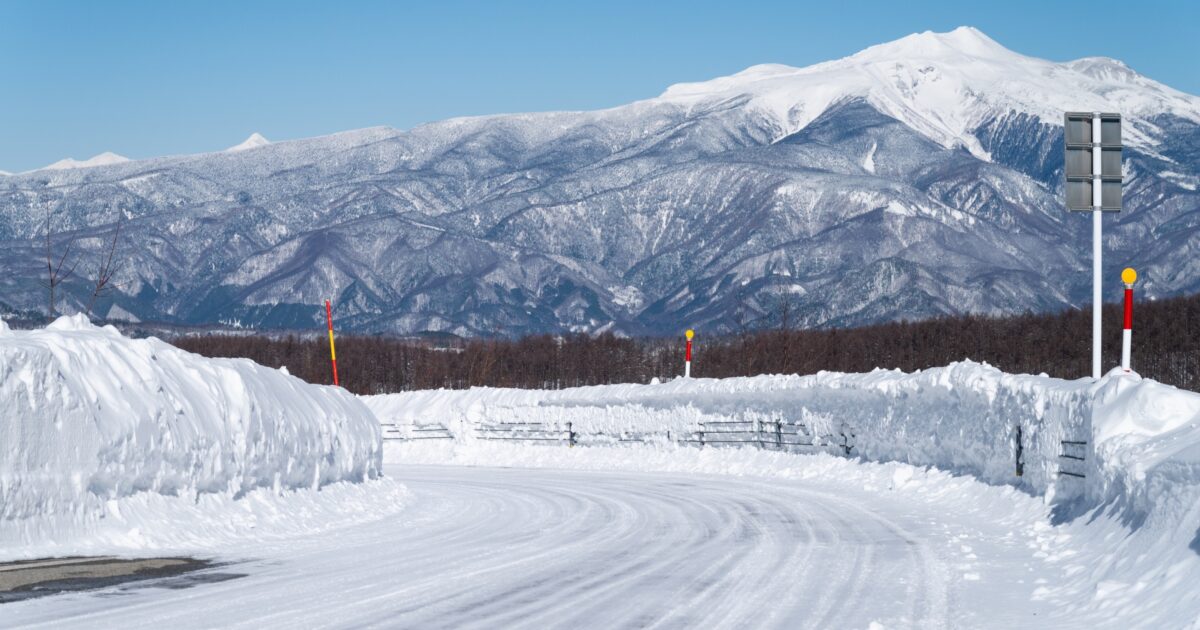雪の壁に囲まれた冬の山道と遠くの雪山