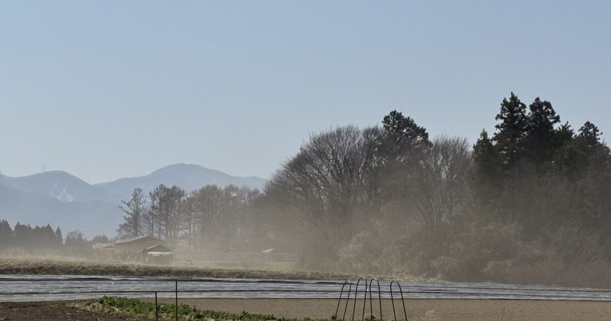 晴天の中でほこりが舞う畑と山の風景
